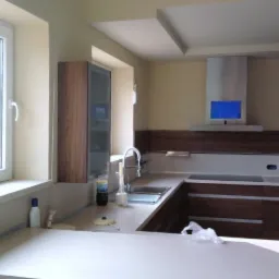 Nowoczesna kuchnia z zabudową karton-gips na suficie, drewniane szafki, biały blat i okap z niebieskim wyświetlaczem.